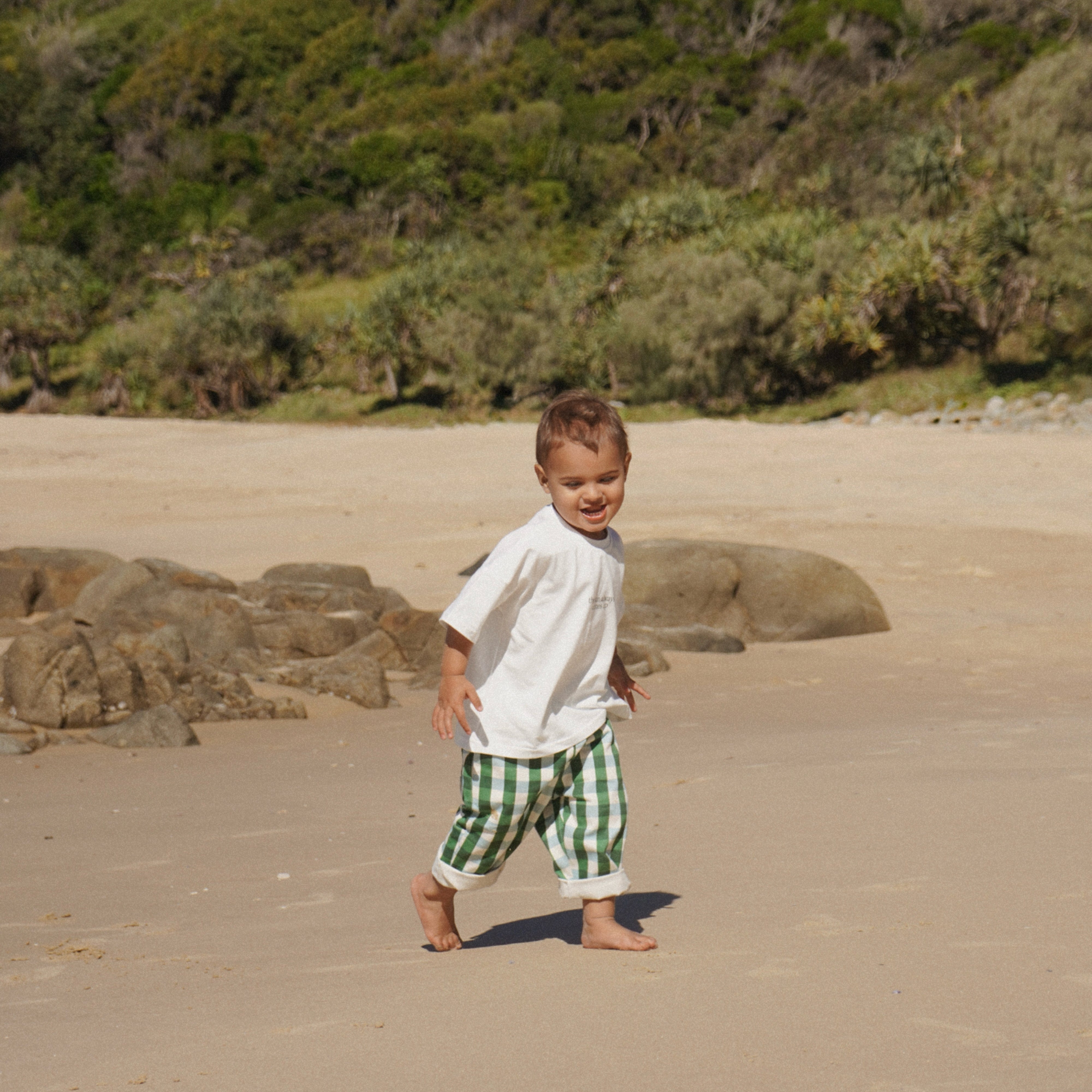 Child walking on a sandy beach with greenery in the background