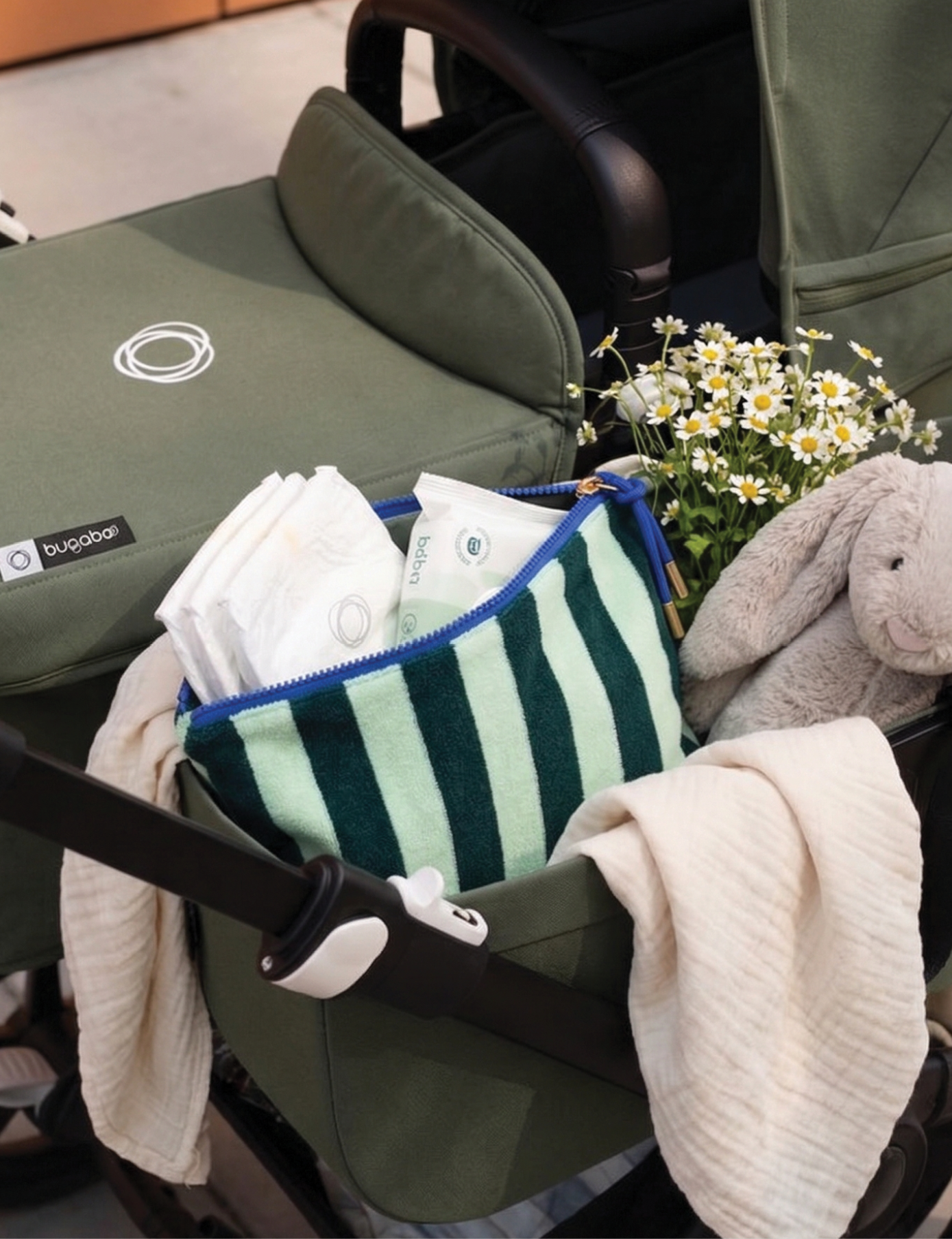 Sonny Label green stripe terrycloth zip pouch inside a pram with daisies, nappies and a soft bunny toy — the perfect nappy bag companion.