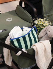 Sonny Label green stripe terrycloth zip pouch inside a pram with daisies, nappies and a soft bunny toy — the perfect nappy bag companion.