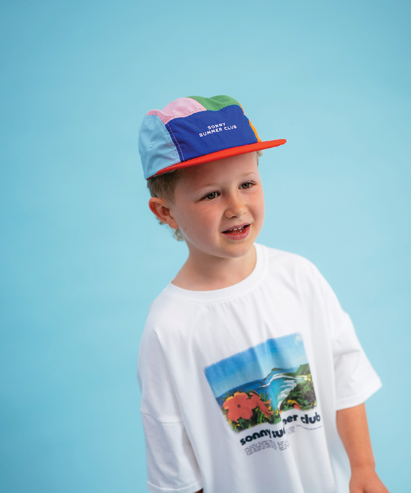 Child in Sonny Label Summer25 playsuit on a vivid sky blue background.
