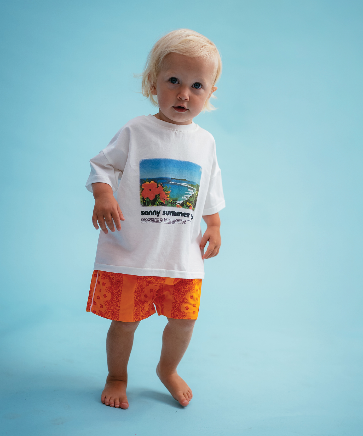 Child wearing Sonny Label Summer25 beach poncho and swimwear on a sky blue background.