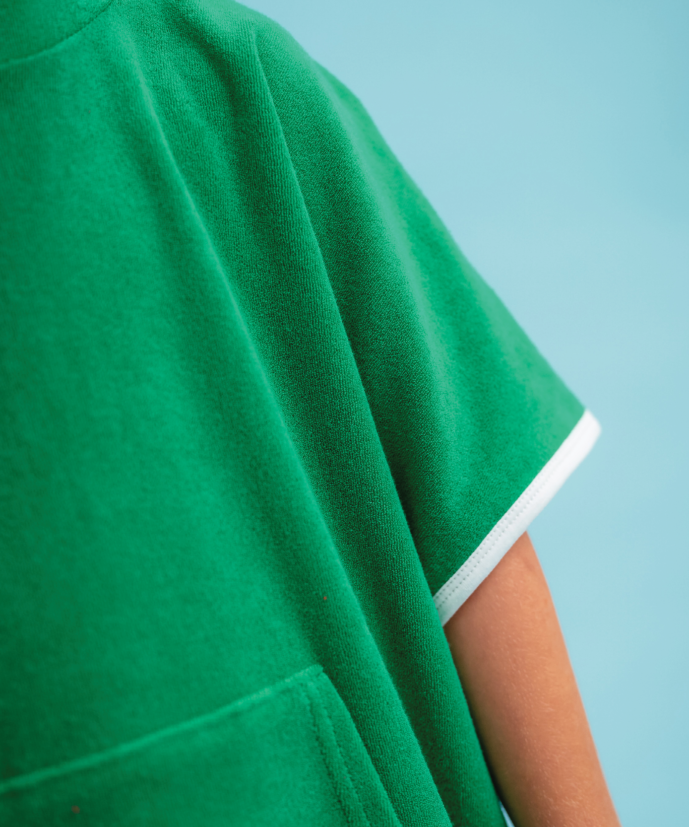 Child wearing Sonny Label Summer25 beach poncho on a vivid sky blue background.