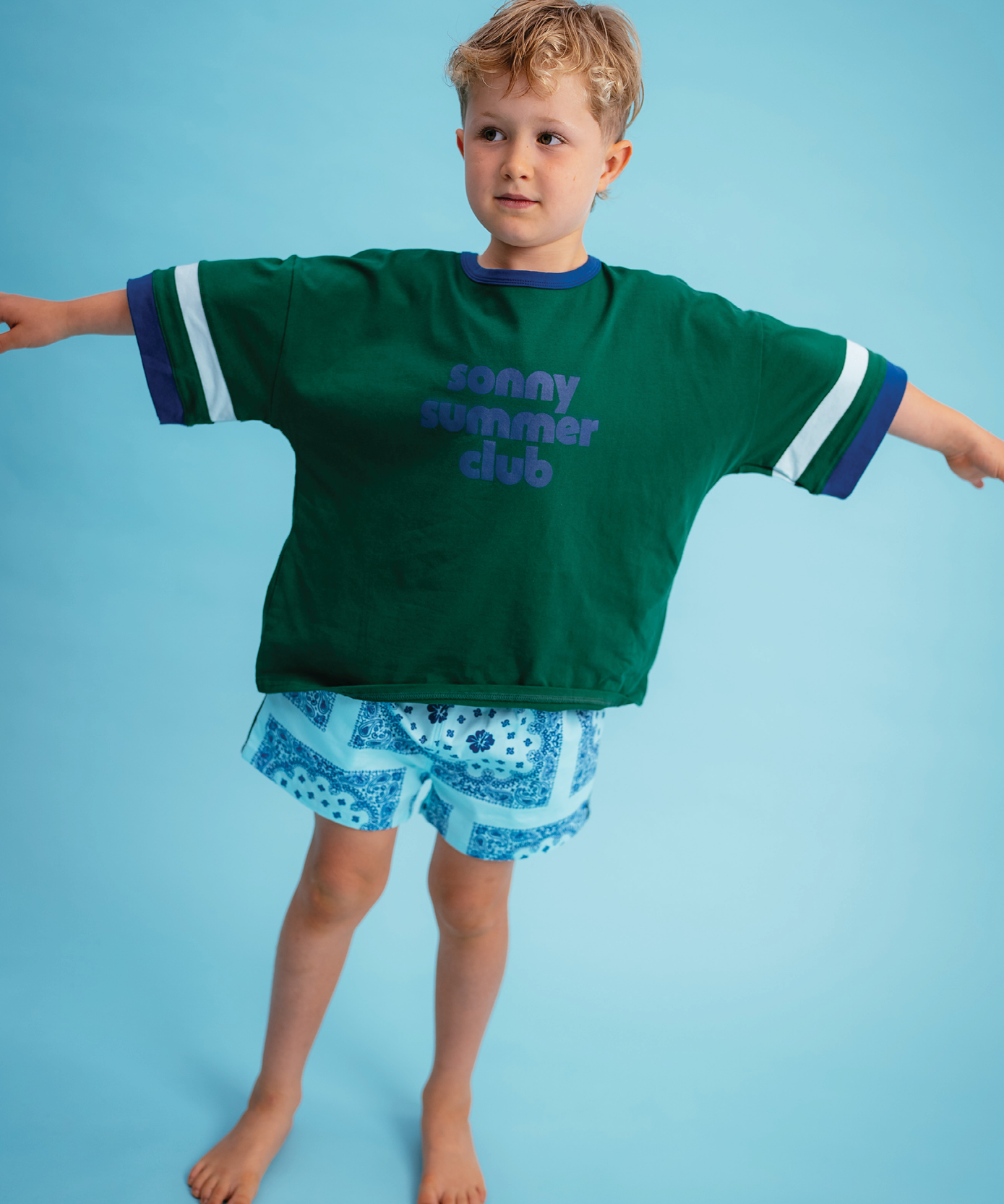 Child in Sonny Label Summer25 collection pieces on a vivid sky blue background.