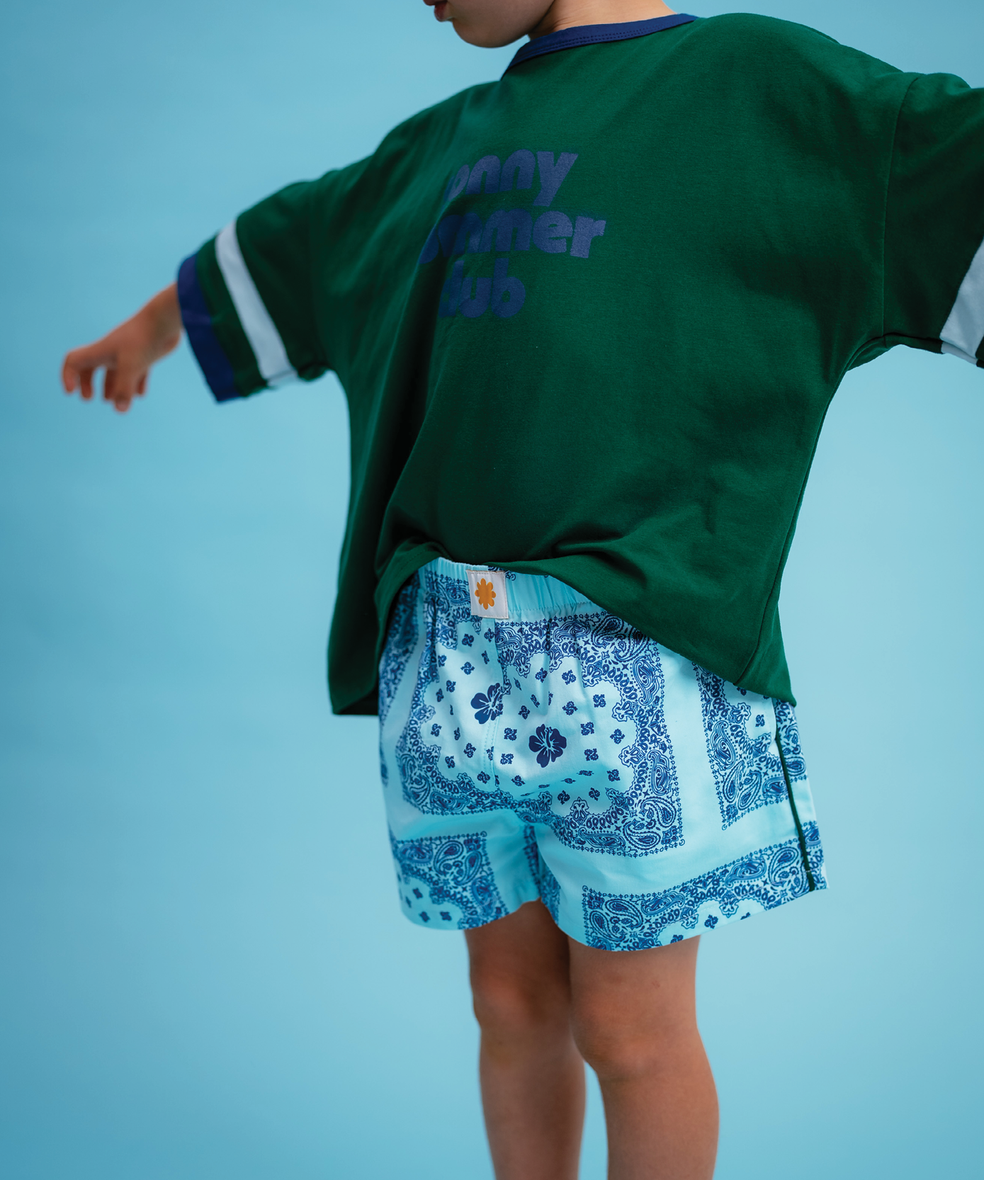 Child wearing Sonny Label Summer25 sport tee and knitted shorties on a sky blue background.