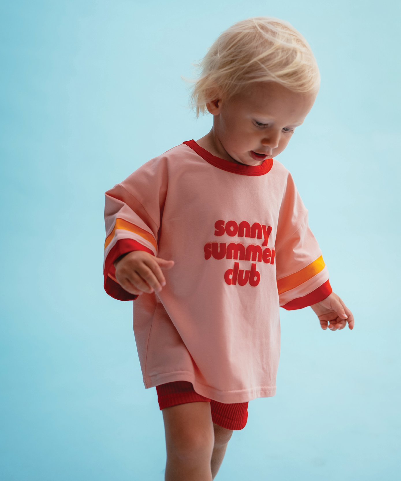 Child in Sonny Label Summer25 summer pieces on a vivid sky blue background.