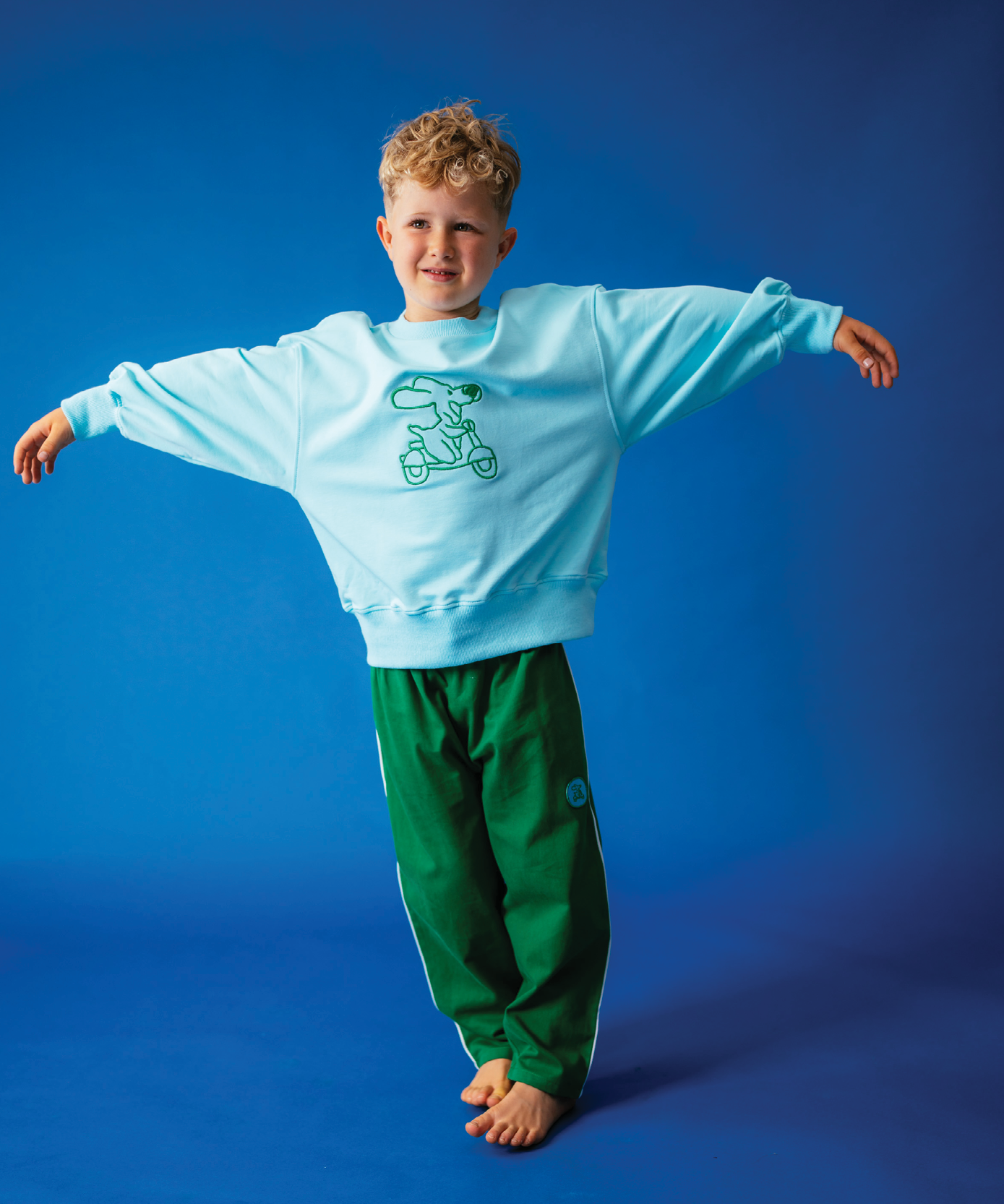 Child in Sonny Label Circus26 collection pieces on a vivid blue background. Variant upload.