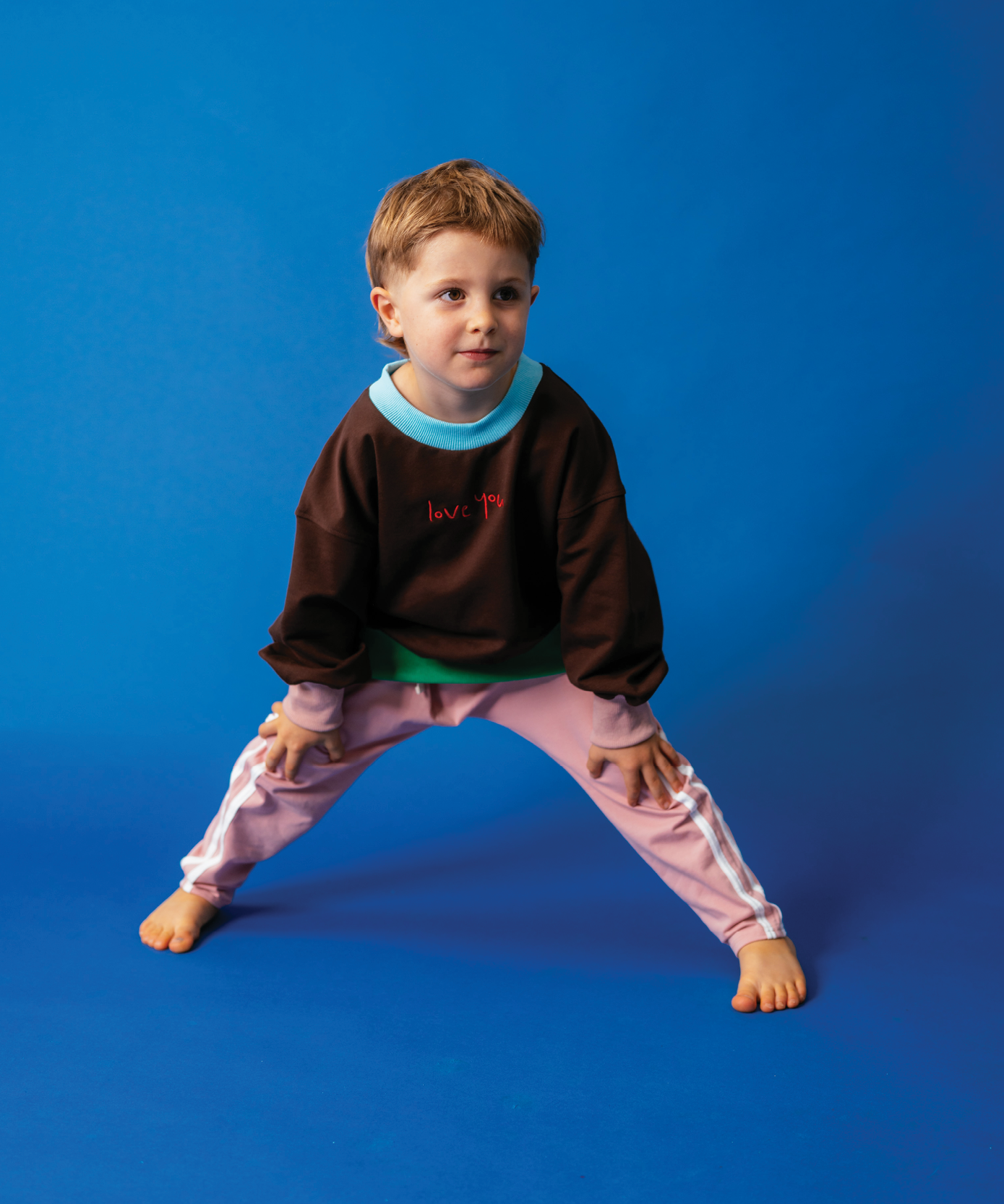 Child wearing Sonny Label Circus26 beanie and sport tee on a deep blue studio backdrop.