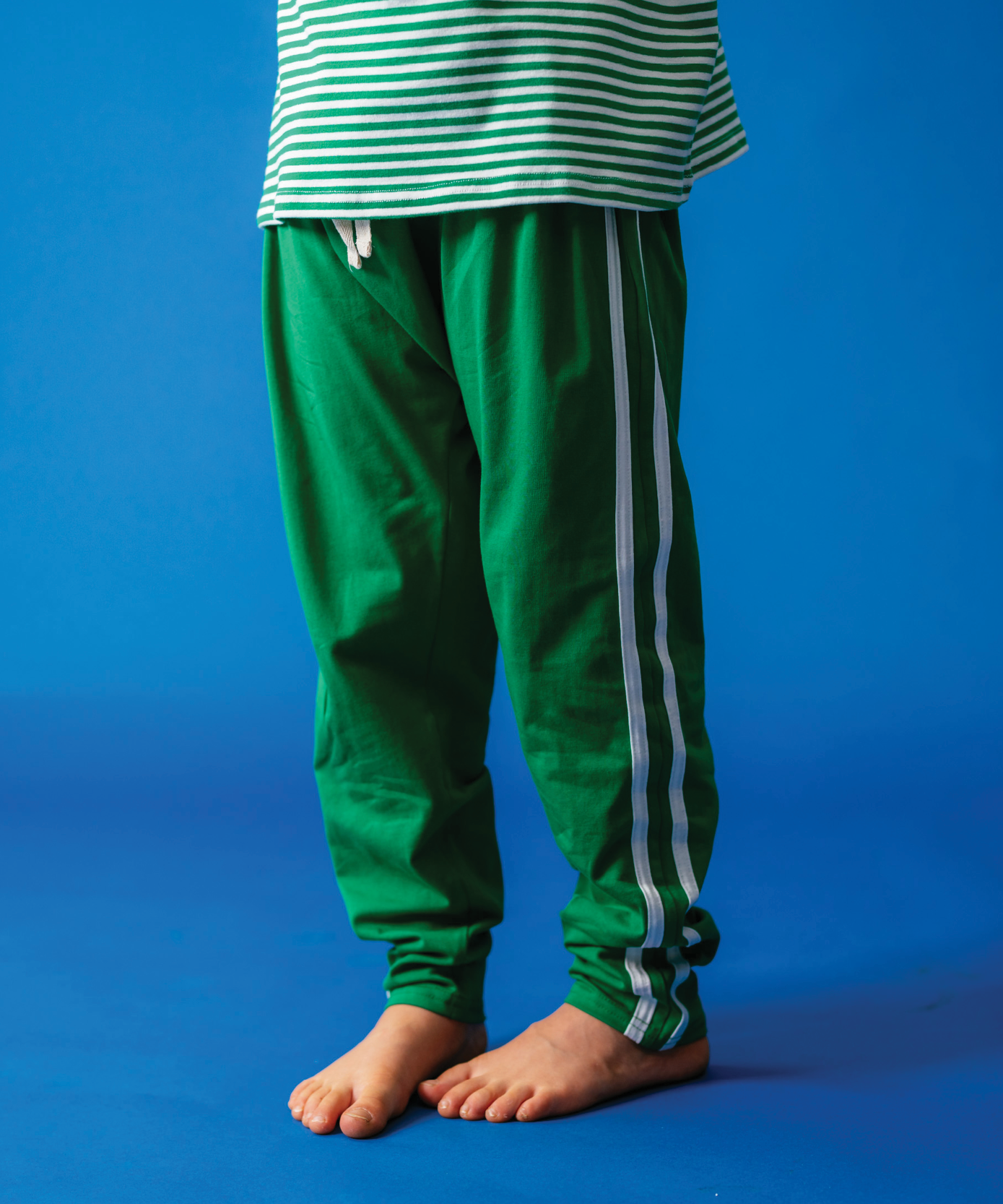 Child wearing Sonny Label Circus26 forest green and white stripe tee and beanie on blue background.