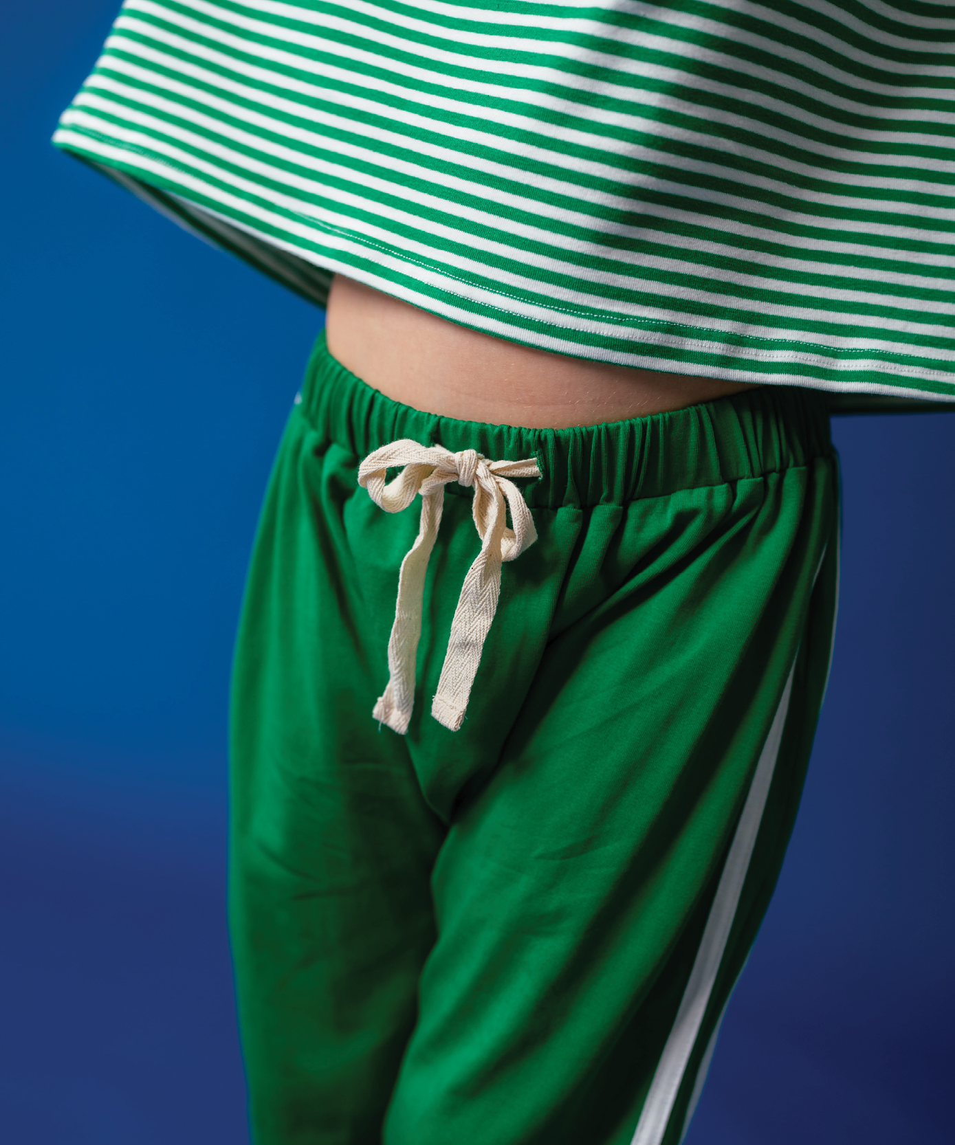 Child wearing Sonny Label Circus26 floss pink beanie and stripe tee on a deep blue backdrop.