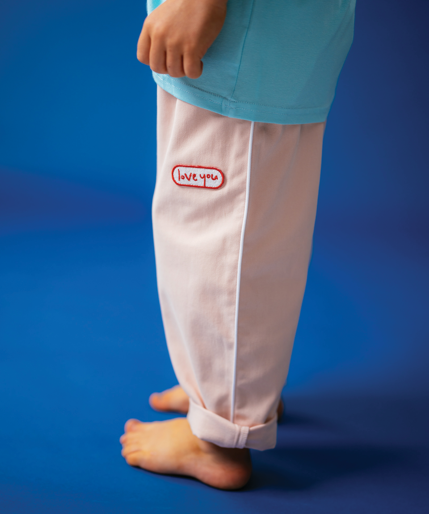 Child in Sonny Label Circus26 stripe long-sleeve tee and forest green sport pants on blue backdrop.