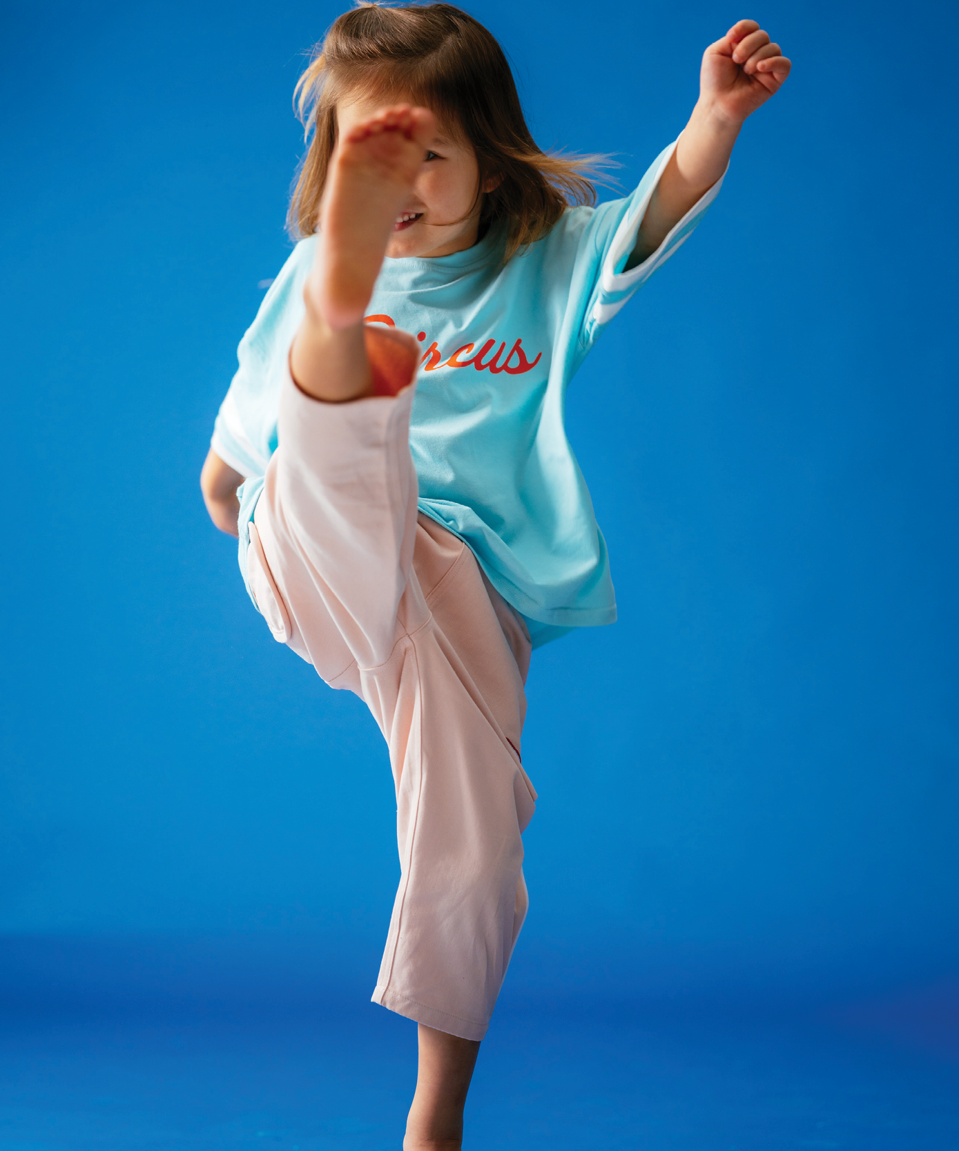 Child wearing Sonny Label Circus26 polka dot pocket pants and sport tee on vivid blue background.