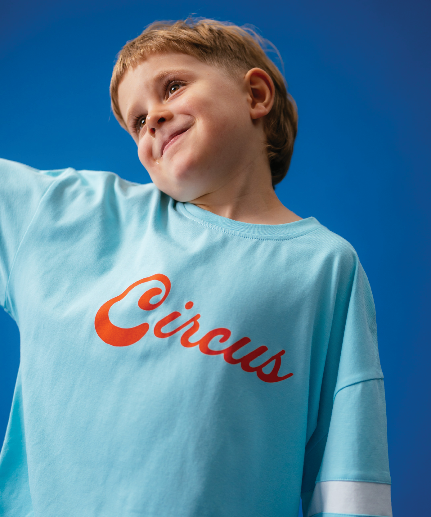 Child wearing Sonny Label Circus26 colourful outfit posed on a deep blue studio background.