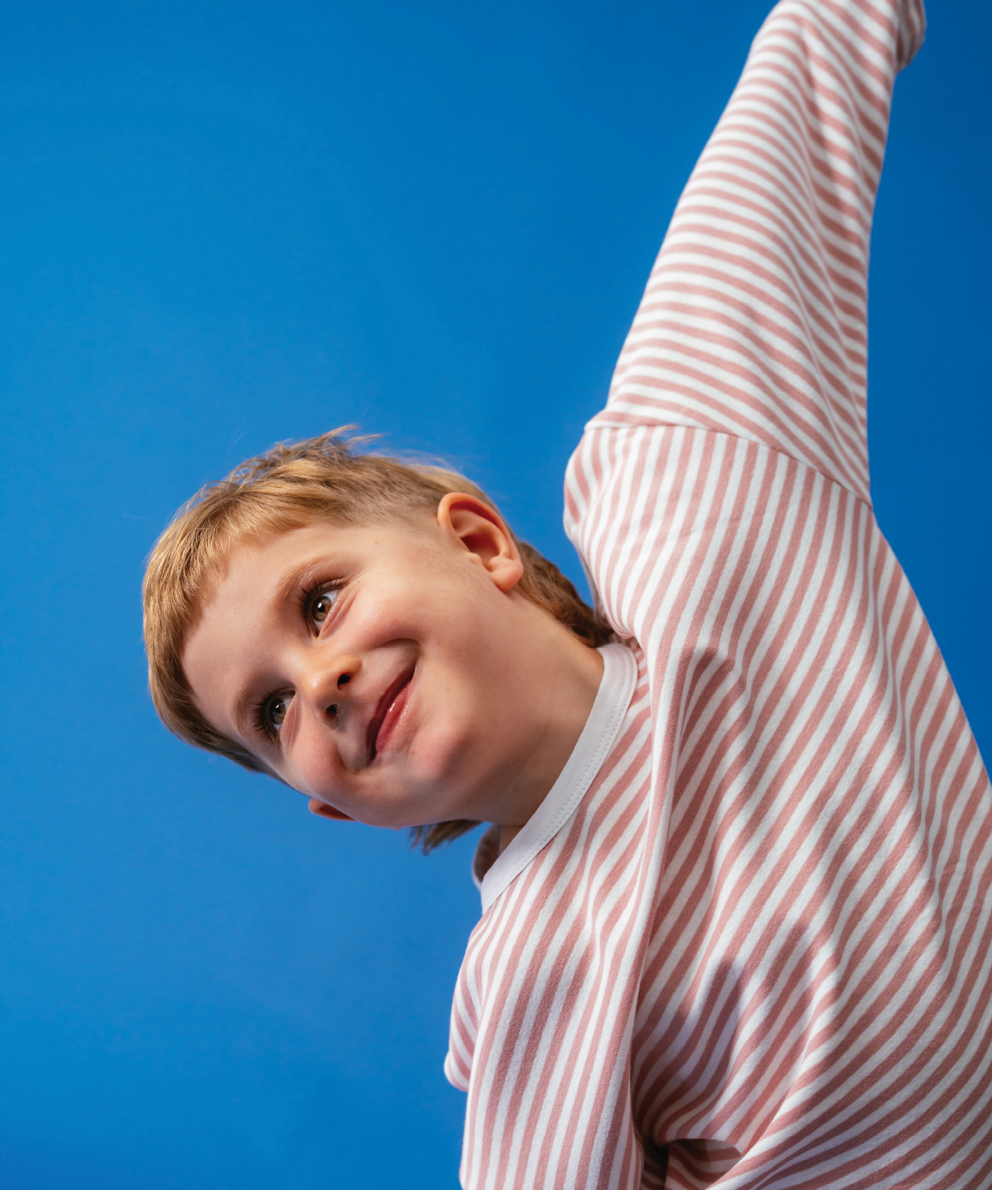 Child in Sonny Label Circus26 forest green sport pants and beanie on a deep blue background.
