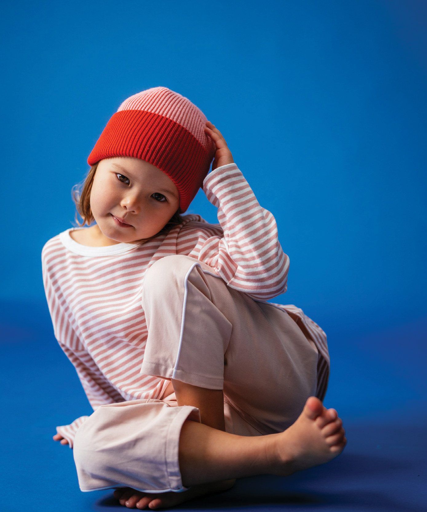 Child wearing Sonny Label Circus26 stripe long-sleeve tee and beanie on a vivid blue backdrop.