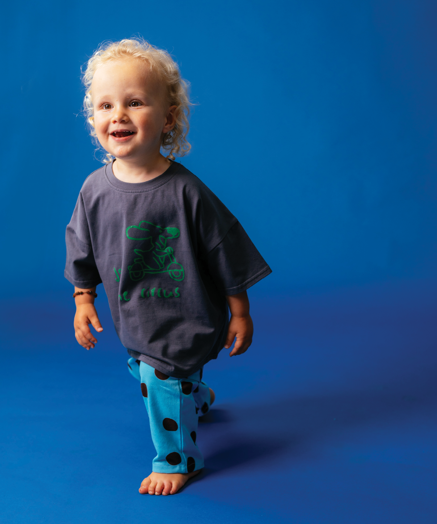 Child wearing Sonny Label Circus26 colourful outfit on a vivid blue studio background.