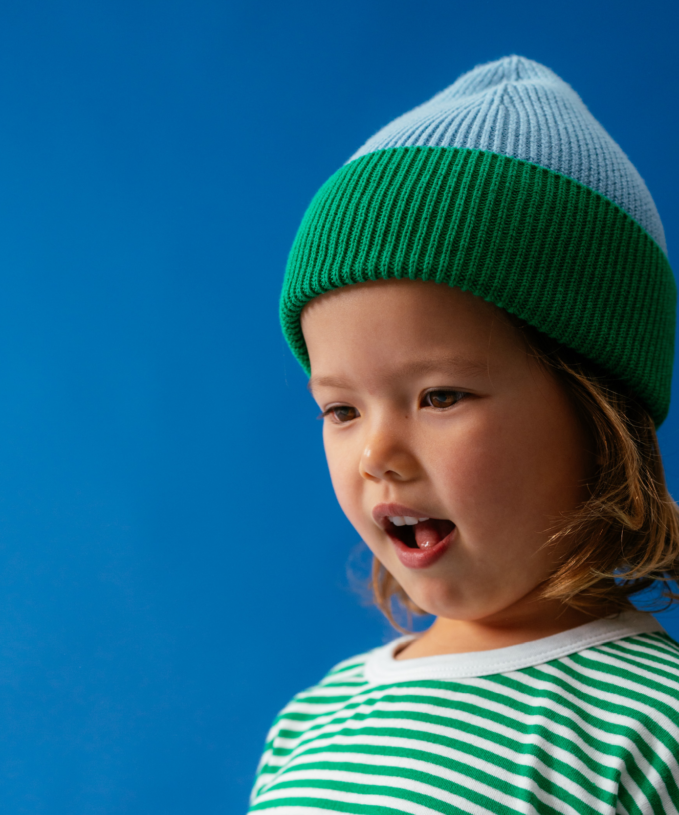 Child in Sonny Label Circus26 sport tee and pants in a playful pose on a vivid blue backdrop.