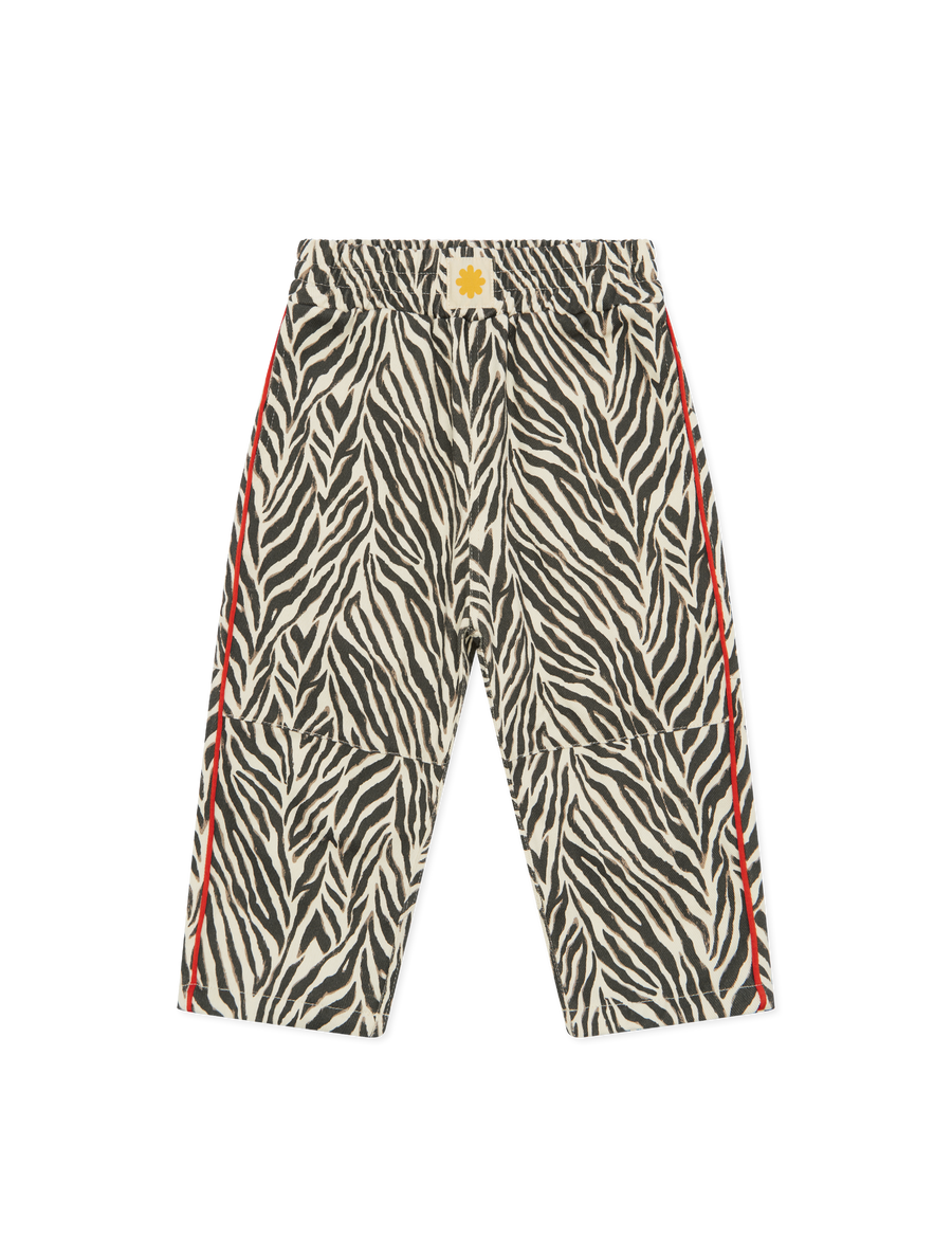 Sonny Label Safari AW25 black and white zebra print wide-leg pocket pants with red stripe and sun badge, flat lay on grey background.